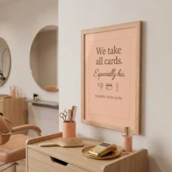 Angled view of the cheeky beauty room framed poster showing the wooden frame depth and blush pink background.