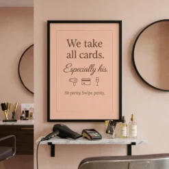 Framed funny blush pink salon payment poster hanging on the wall above a stylish hair stylist station in a beauty room